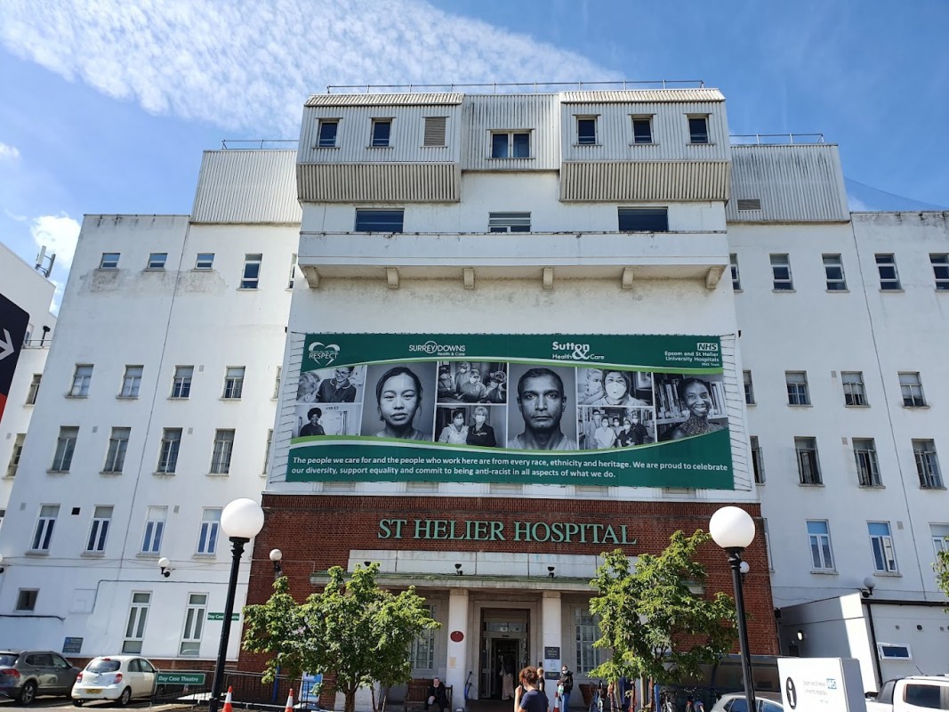 Το δημόσιο νοσοκομείο St. Helier στον δήμο του Σάτον του Λονδίνου όπου έργαζεται ο Βελεστινιώτης γιατρός διευθύνεται από τα Πανεπιστημιακά Νοσοκομεία Epsom και St Helier NHS Trust μαζί με το νοσοκομείο Epsom. Βρίσκεται δίπλα στο μεγάλο δημοτικό κτήμα του St Helier και κοντά στη μεγάλη διασταύρωση που είναι γνωστή ως Rosehill.